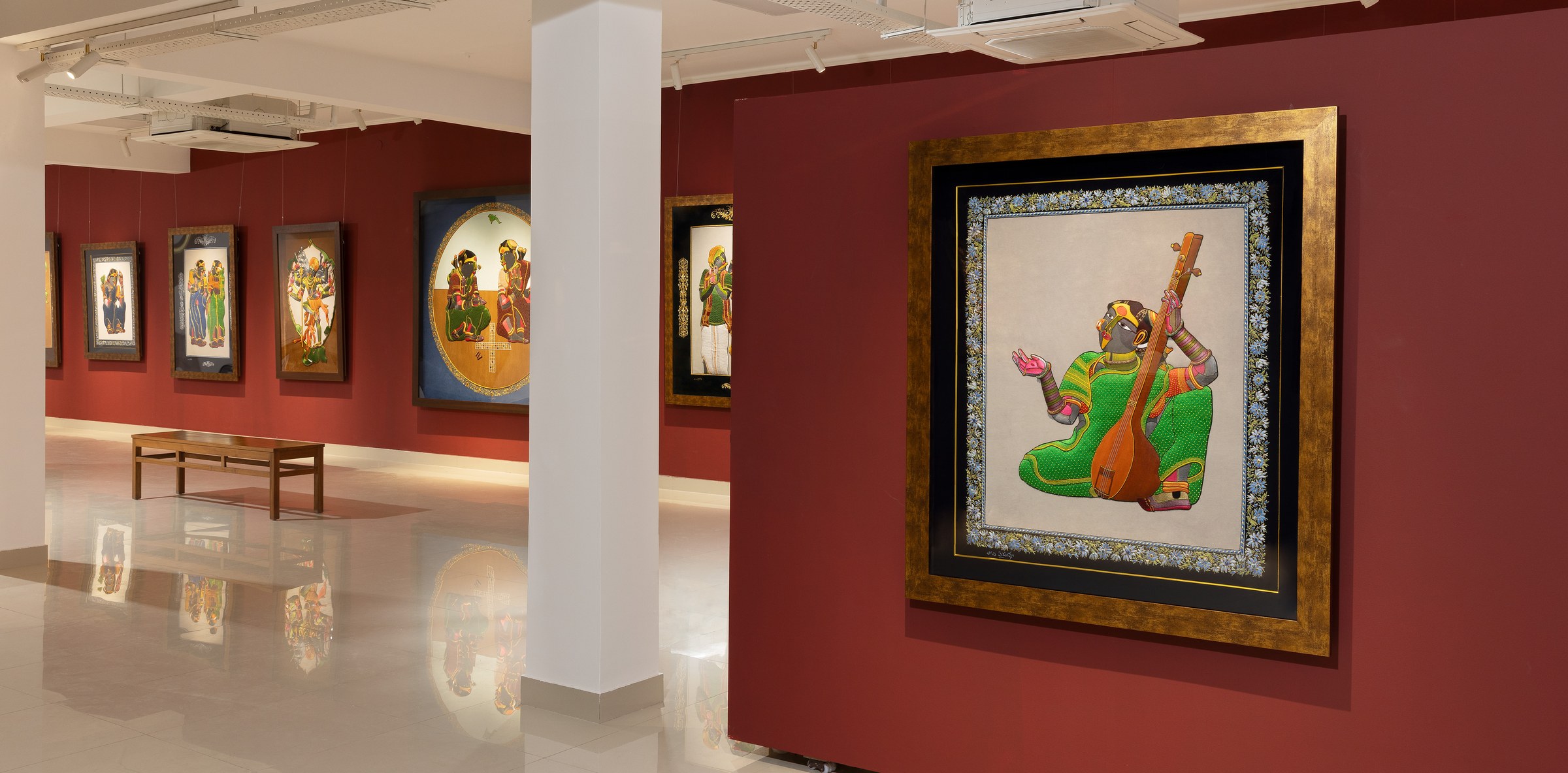Installation view of Threads of Tradition: framed zardozi embroideries after Thota Vaikuntam paintings hung on deep red gallery walls