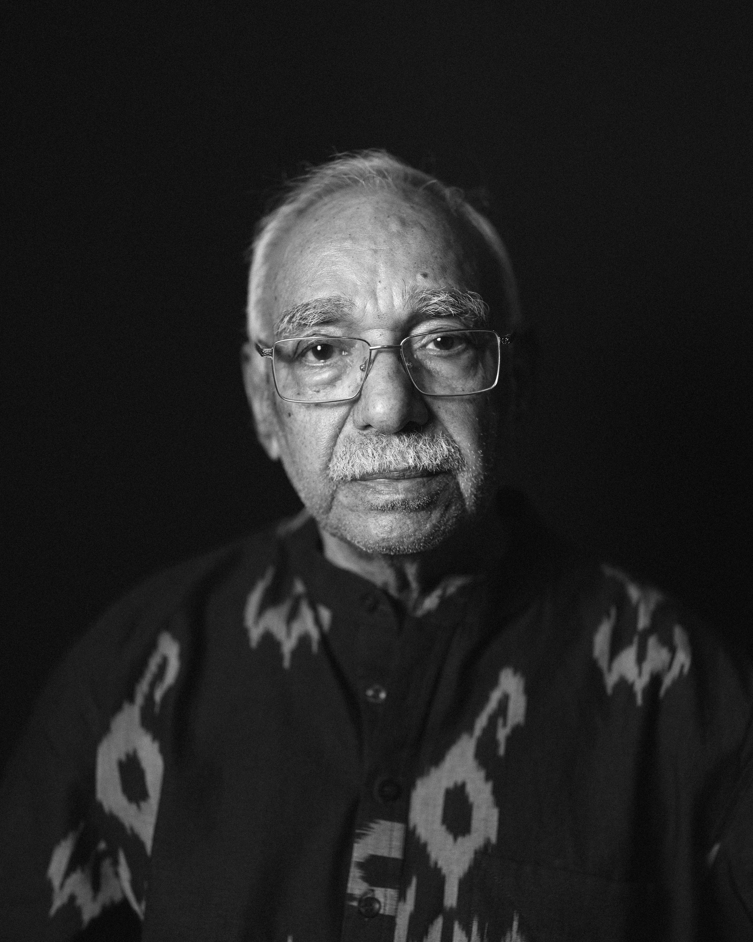 Black-and-white portrait of Thota Vaikuntam in glasses and a patterned ikat shirt against a black background