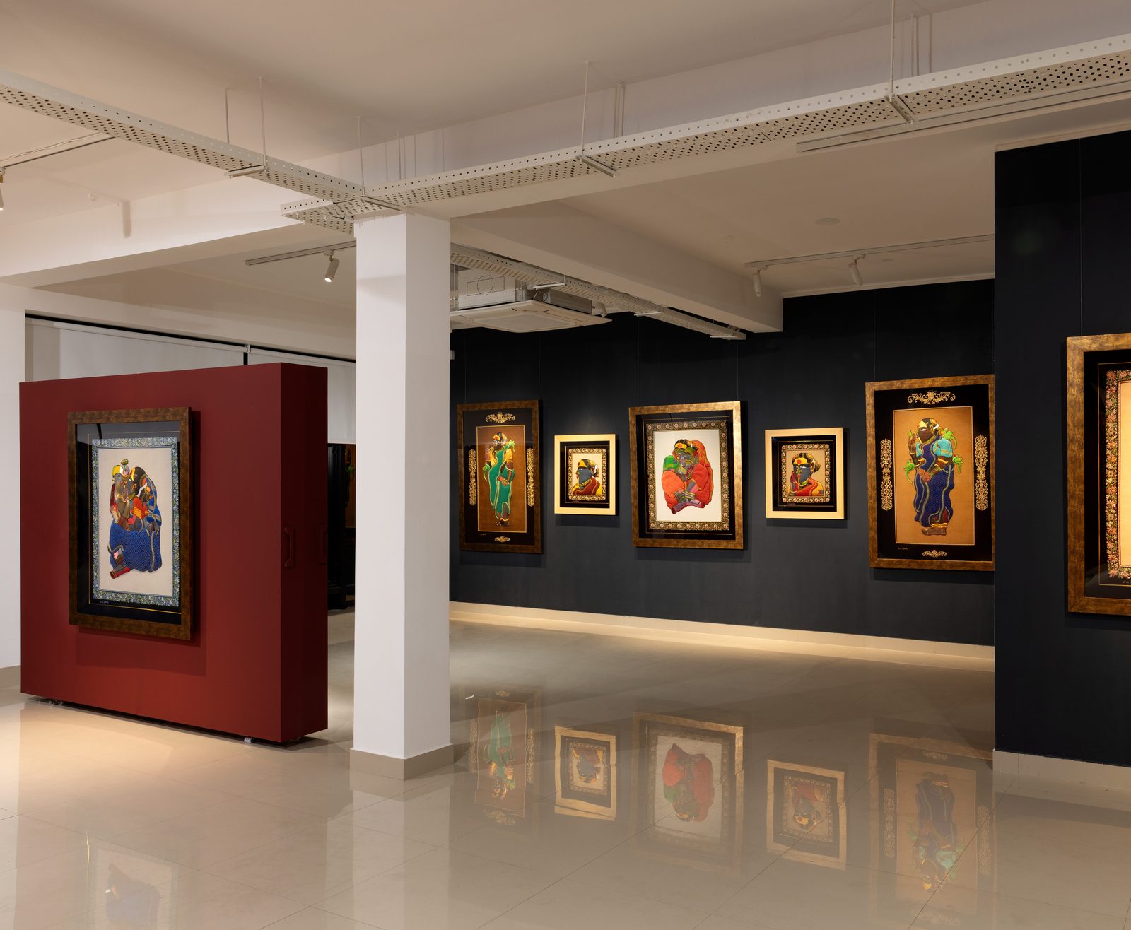 Installation view of an exhibition of Thota Vaikuntam's zardozi embroideries: framed works on a dark wall and one on a freestanding red panel in a white gallery