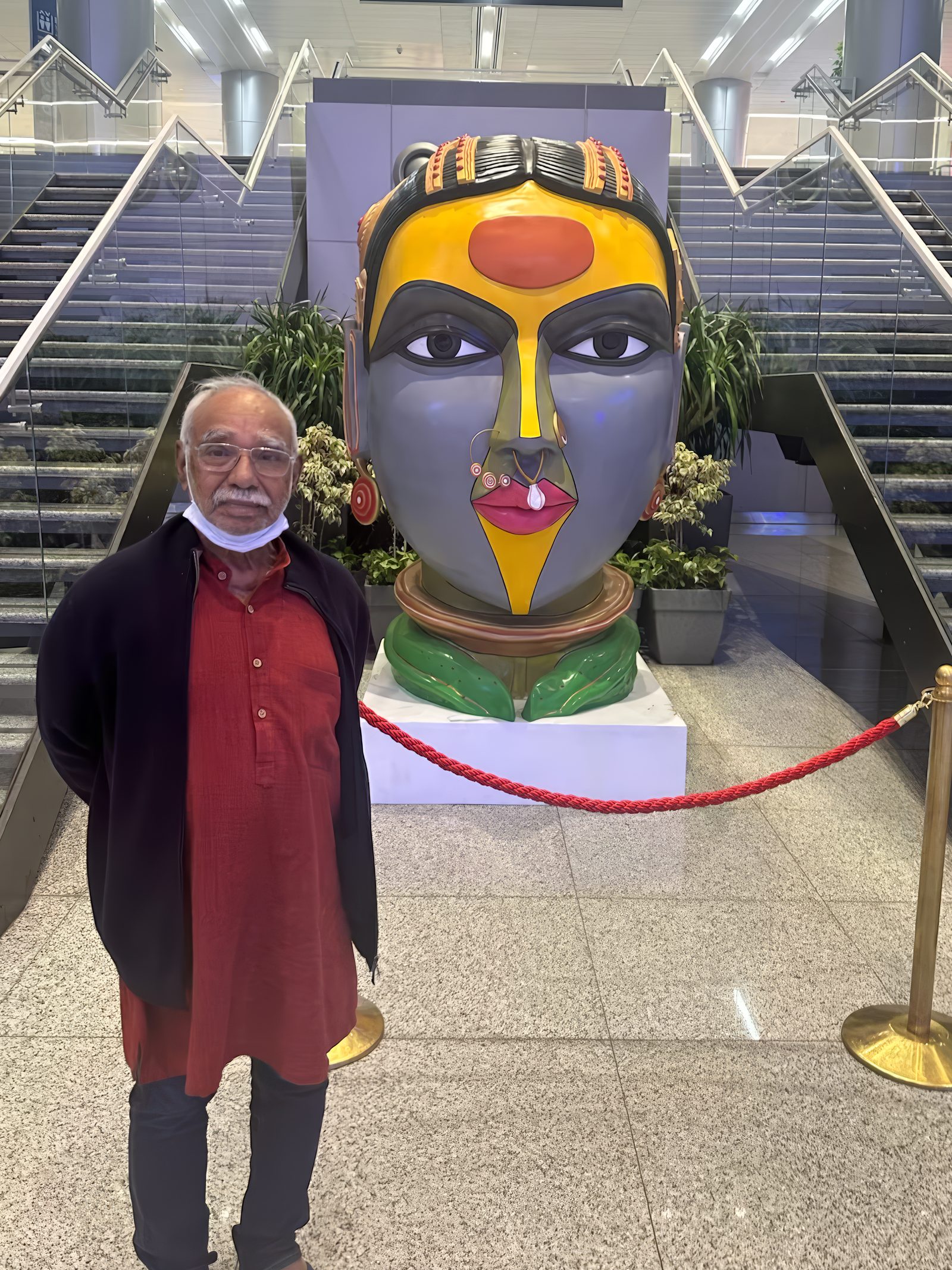 Thota Vaikuntam beside his monumental painted fibreglass head of a Telangana woman, garlanded and cordoned by a red rope at the foot of a staircase inside Rajiv Gandhi International Airport, Hyderabad
